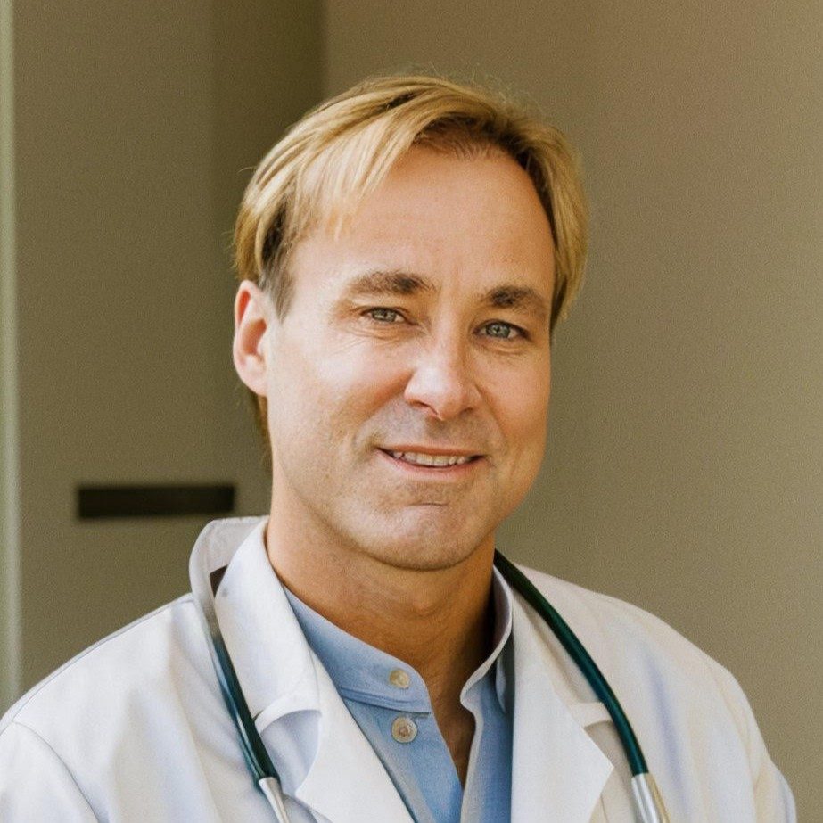 MD, PA-C Thousand Oaks CA Scott Mortensen Meet The Team Dr. Scott Mortensen smiling in front of a tan wall wearing a white jacket